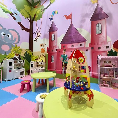 Evergreen Laurel Hotel - Тайджун Екстериор снимка The photo shows a colorful children's playroom designed with a whimsical theme. The walls are painted in bright colors and feature a cartoon-style mural of a pink castle with purple towers and a smiling cartoon elephant. The room is filled with playf