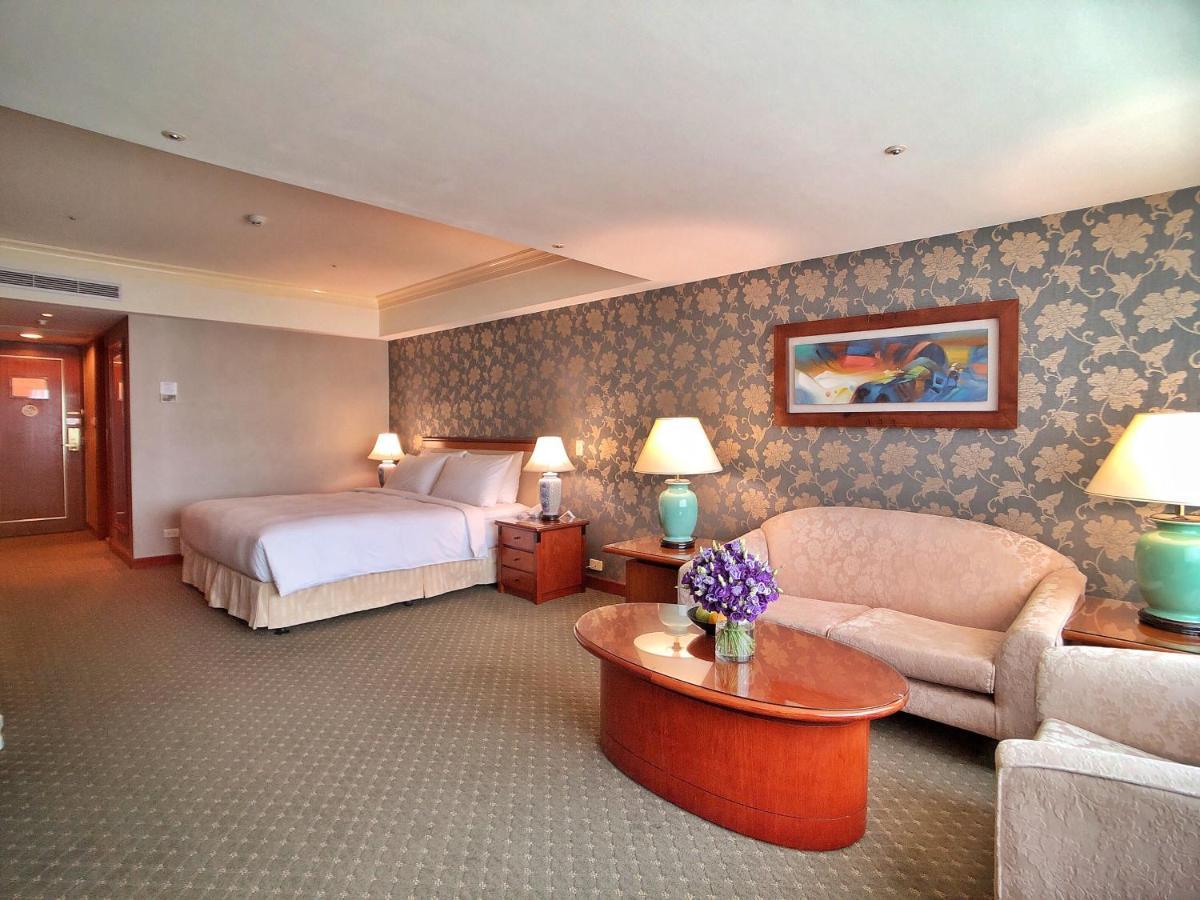 Evergreen Laurel Hotel - Тайджун Екстериор снимка The photo shows a hotel room that features a well-furnished space. It includes a large bed with a light-colored bedspread, a comfortable sofa, and armchair. There's a coffee table with a vase of flowers in the center. The room has a decorative wallpa