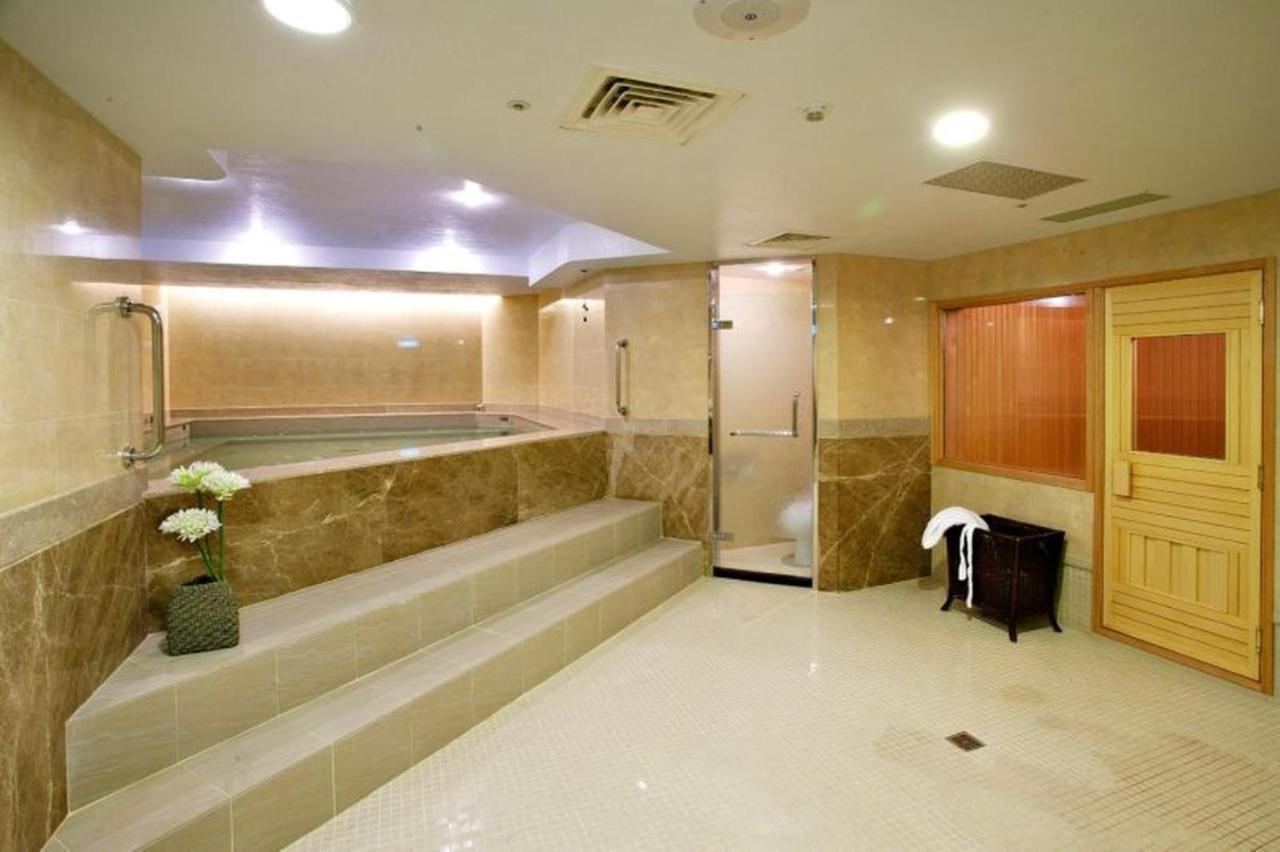 Evergreen Laurel Hotel - Тайджун Екстериор снимка The photo shows a spacious and well-lit spa or wellness area. It features a large, recessed hot tub with steps leading up to it, surrounded by beige marble walls. There's a shower area enclosed in glass, and to the right, a wooden sauna or steam room