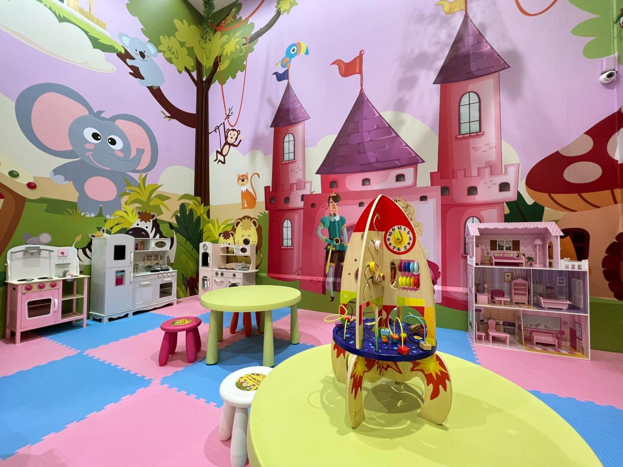 Evergreen Laurel Hotel - Тайджун Екстериор снимка The photo shows a colorful children's playroom designed with a whimsical theme. The walls are painted in bright colors and feature a cartoon-style mural of a pink castle with purple towers and a smiling cartoon elephant. The room is filled with playf