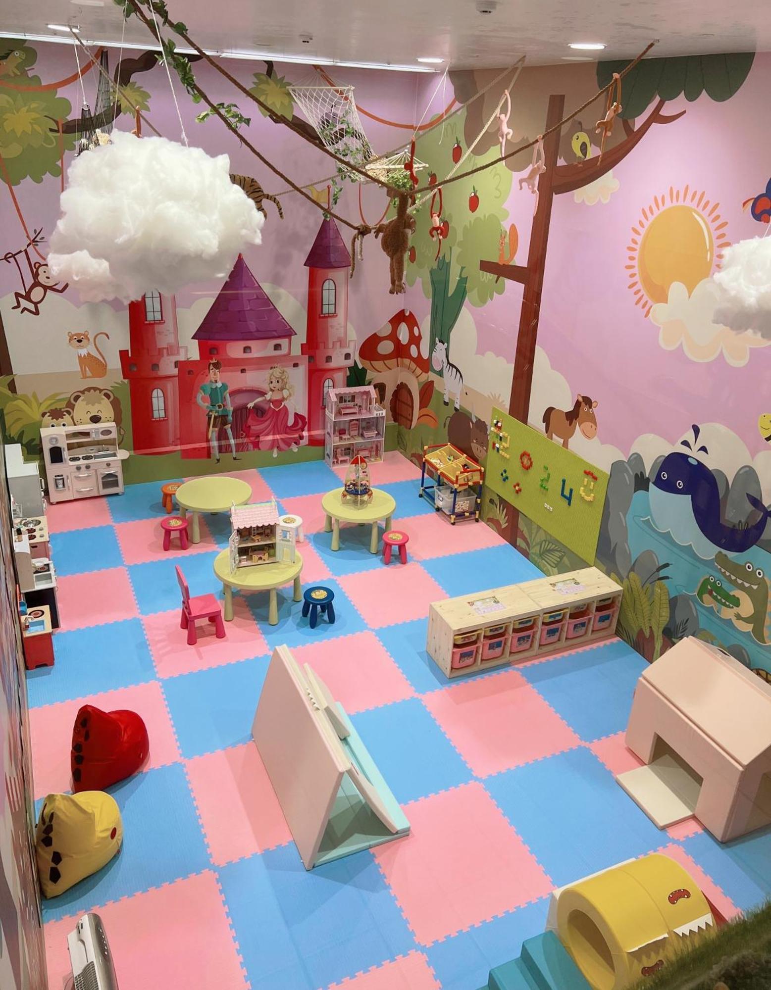 Evergreen Laurel Hotel - Тайджун Екстериор снимка The photo shows a colorful playroom designed for children. It features a vibrant mural with a fairytale castle, trees, and playful animals on the walls. The floor is covered with interlocking foam tiles in pink and blue, providing a soft play surface