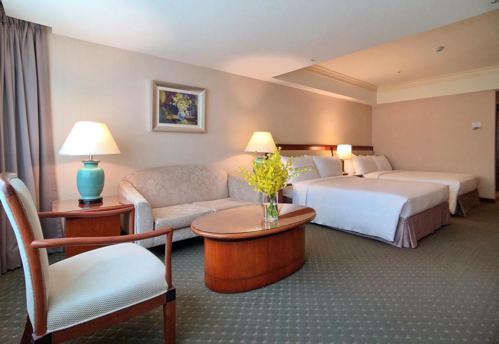 Evergreen Laurel Hotel - Тайджун Екстериор снимка The photo shows a hotel room featuring two beds, a small seating area, and a coffee table. The walls are painted in soft, neutral colors, and there is a framed piece of artwork hanging on the wall. A potted plant with yellow flowers is placed on the 
