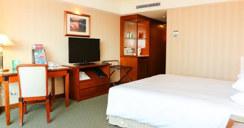 Evergreen Laurel Hotel - Тайджун Екстериор снимка The photo shows a hotel room featuring a neatly made bed with a white blanket. On one side, there is a wooden desk with a chair, and a flat-screen television is mounted nearby. An accent cabinet is visible, displaying various items. The walls are pai
