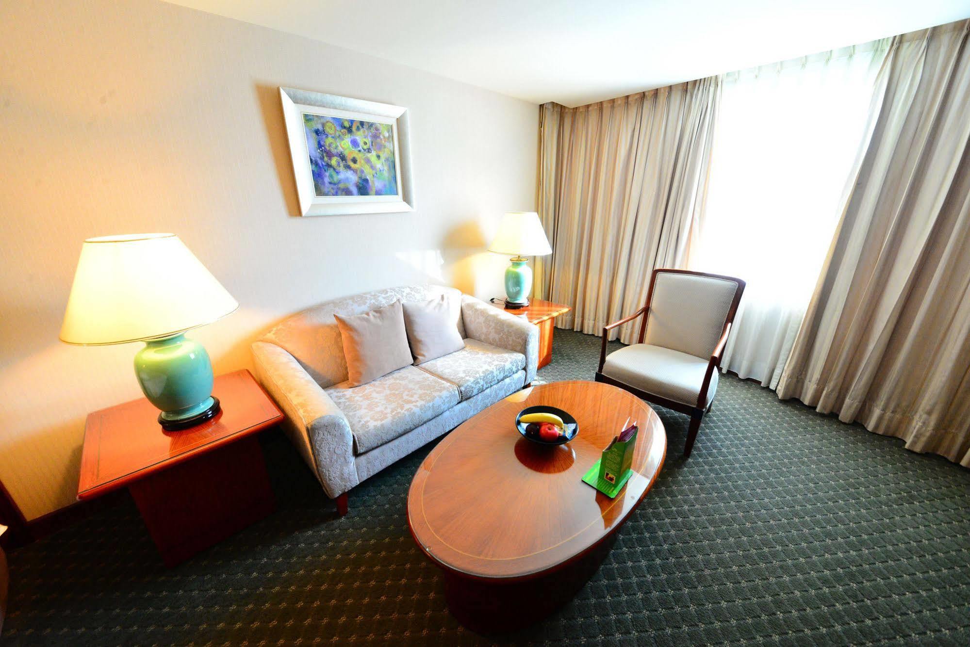 Evergreen Laurel Hotel - Тайджун Екстериор снимка The photo shows a cozy living space, likely a hotel room or a lounge area. It features a light-colored sofa with cushions, a wooden coffee table in the center, and a comfortable armchair beside it. There are two lamps with turquoise bases on side tab
