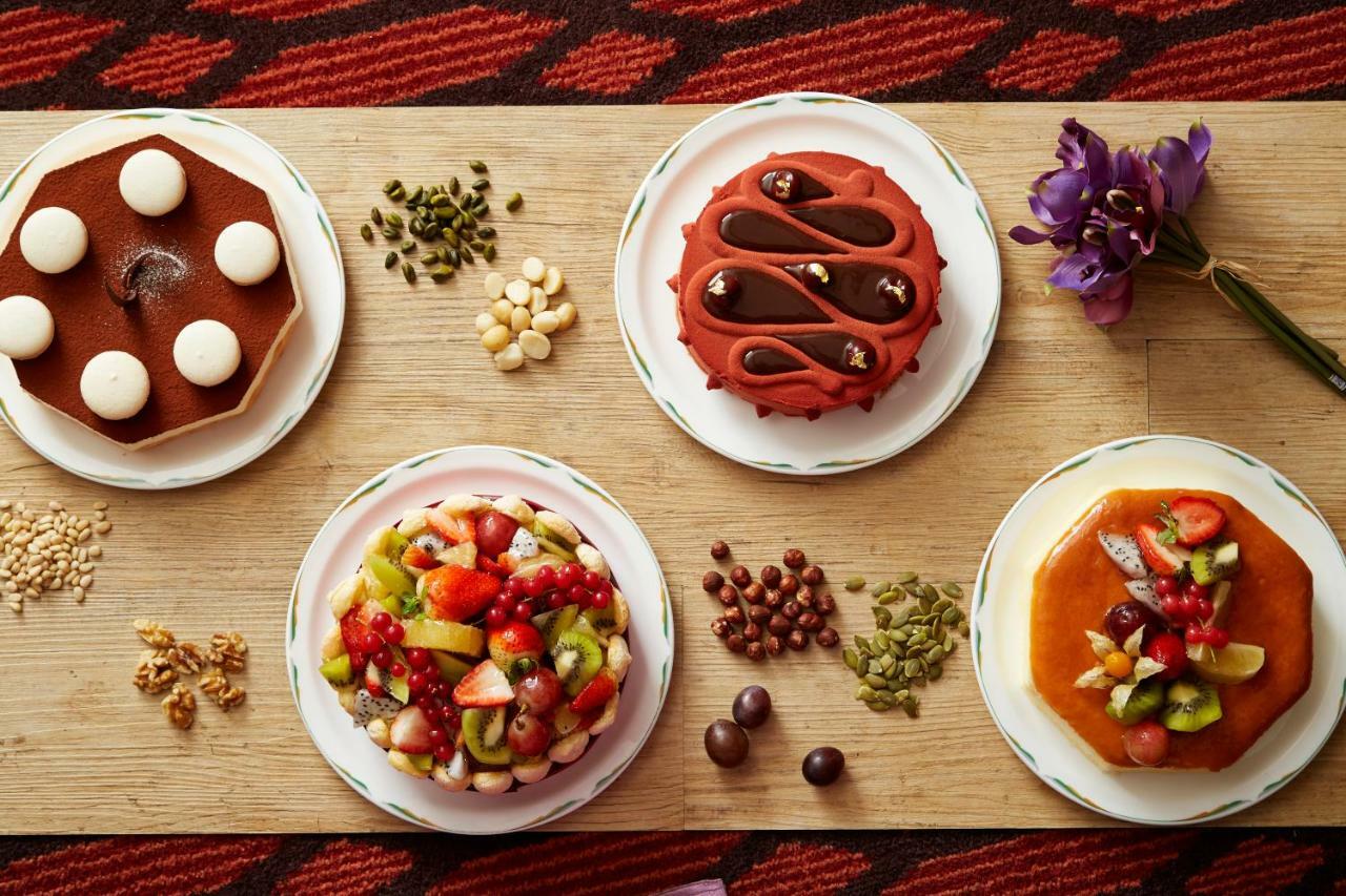 Evergreen Laurel Hotel - Тайджун Екстериор снимка The photo displays a variety of desserts arranged on small plates. There are three main cakes or tarts:

1. **Top Left Plate**: A round chocolate cake with a smooth surface and white decorations on top.
2. **Top Middle Plate**: Another cake, possibly