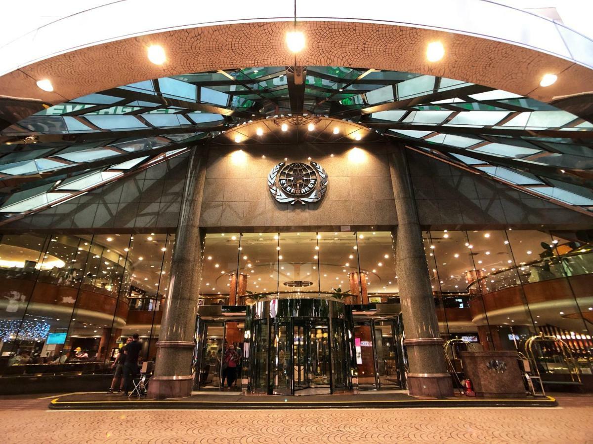 Evergreen Laurel Hotel - Тайджун Екстериор снимка The image shows the entrance of a modern building, likely a hotel or a luxury establishment. The entrance features a large revolving door surrounded by glass panels. Above the entrance, there is a prominent logo or emblem. The overall architectural d