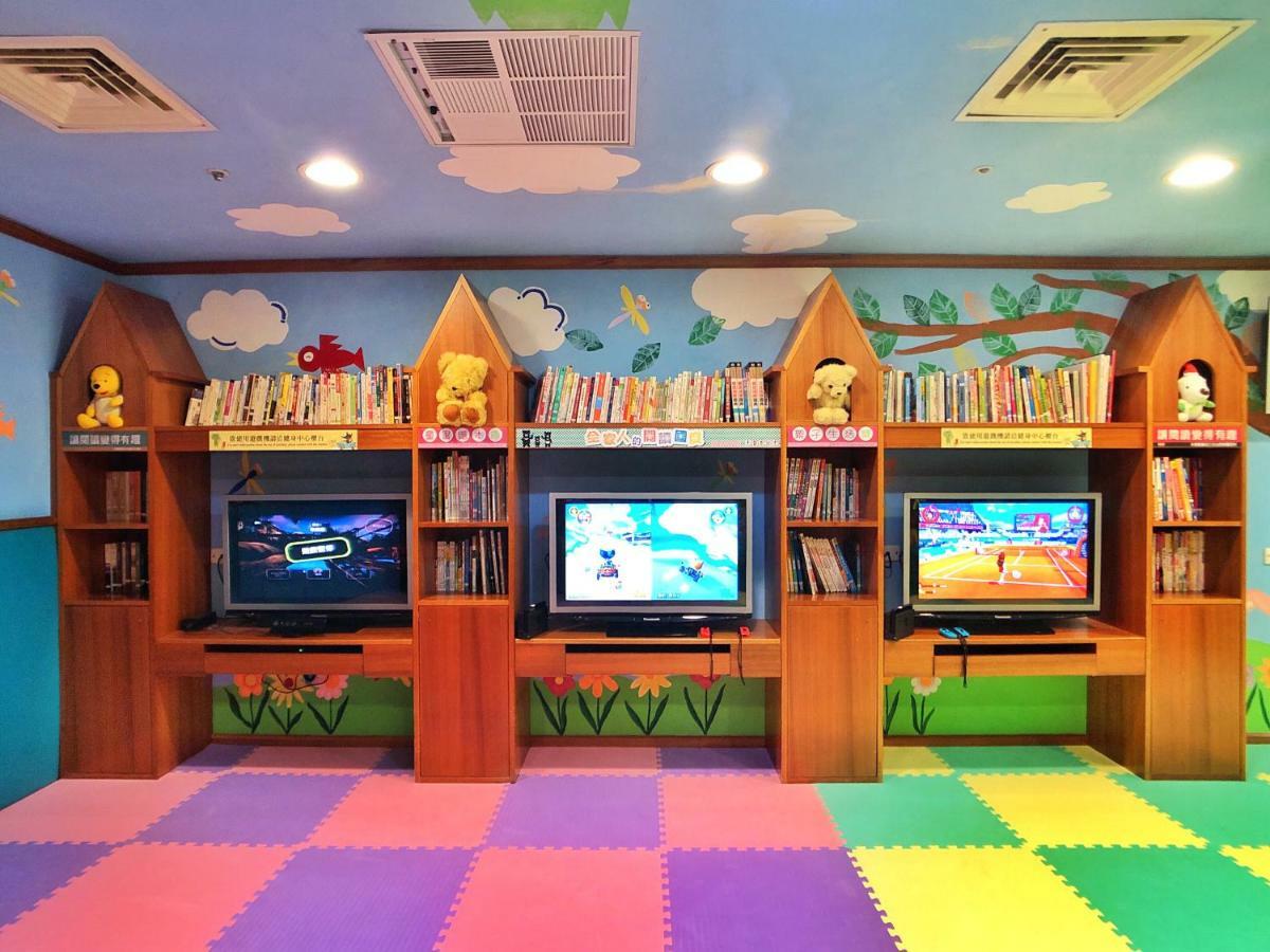 Evergreen Laurel Hotel - Тайджун Екстериор снимка The photo shows a colorful and playful room designed for children. In the center, there are three wooden gaming stations, each equipped with a television screen and surrounded by shelves filled with books. The walls are decorated with cheerful images