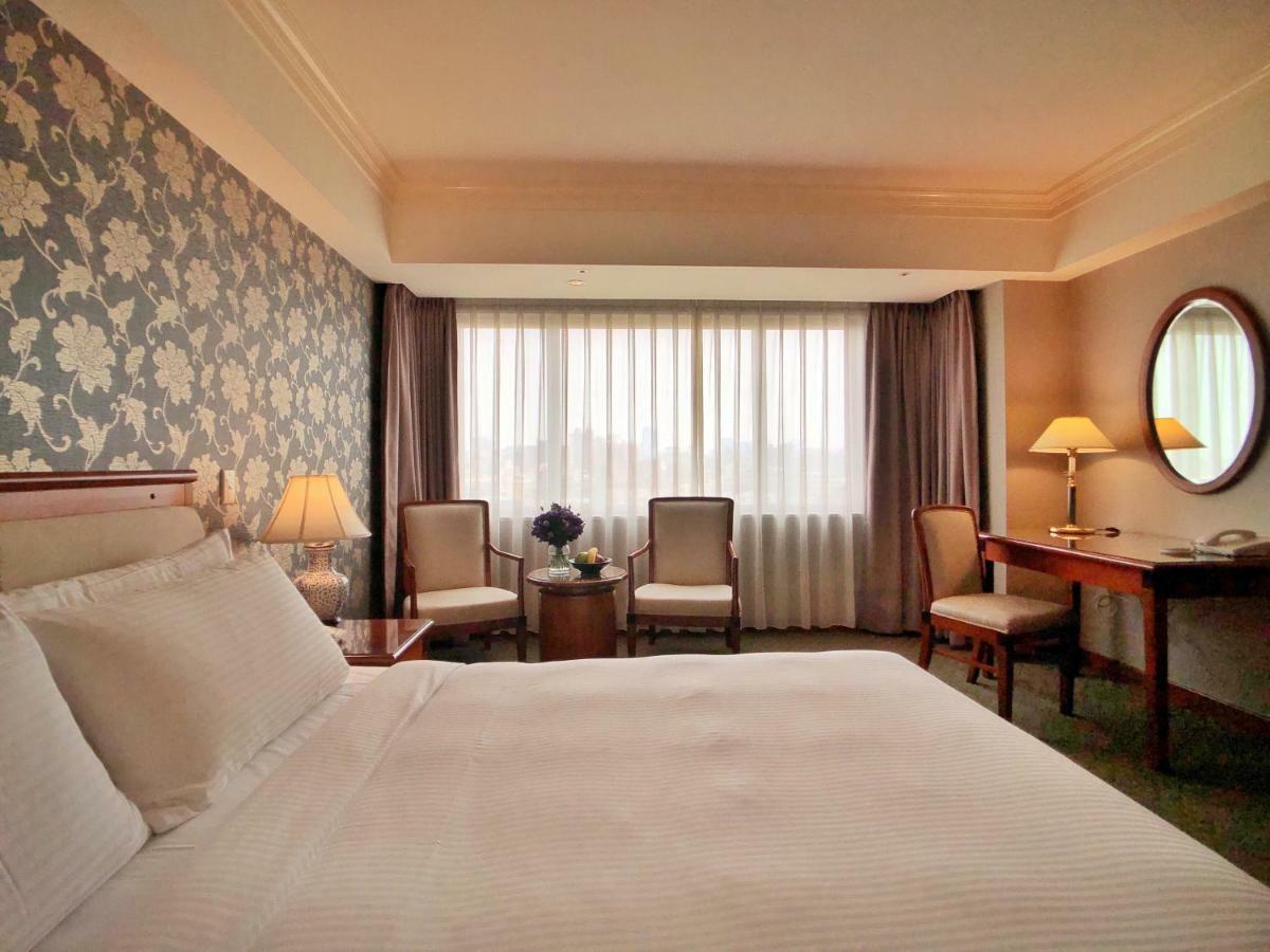 Evergreen Laurel Hotel - Тайджун Екстериор снимка The photo shows a hotel room with a comfortable and inviting design. There is a large bed with crisp white bedding on the left side of the image. To the right, there are two elegant chairs with a small round table between them, adorned with a bouquet