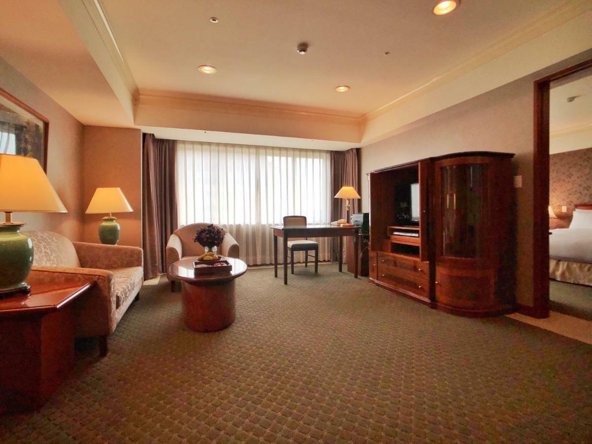 Evergreen Laurel Hotel - Тайджун Екстериор снимка The photo shows a cozy hotel suite or living area. There is a sofa and an armchair arranged around a small coffee table. A desk with a chair is positioned near a large window covered with sheer curtains that allow natural light to enter the room. Two