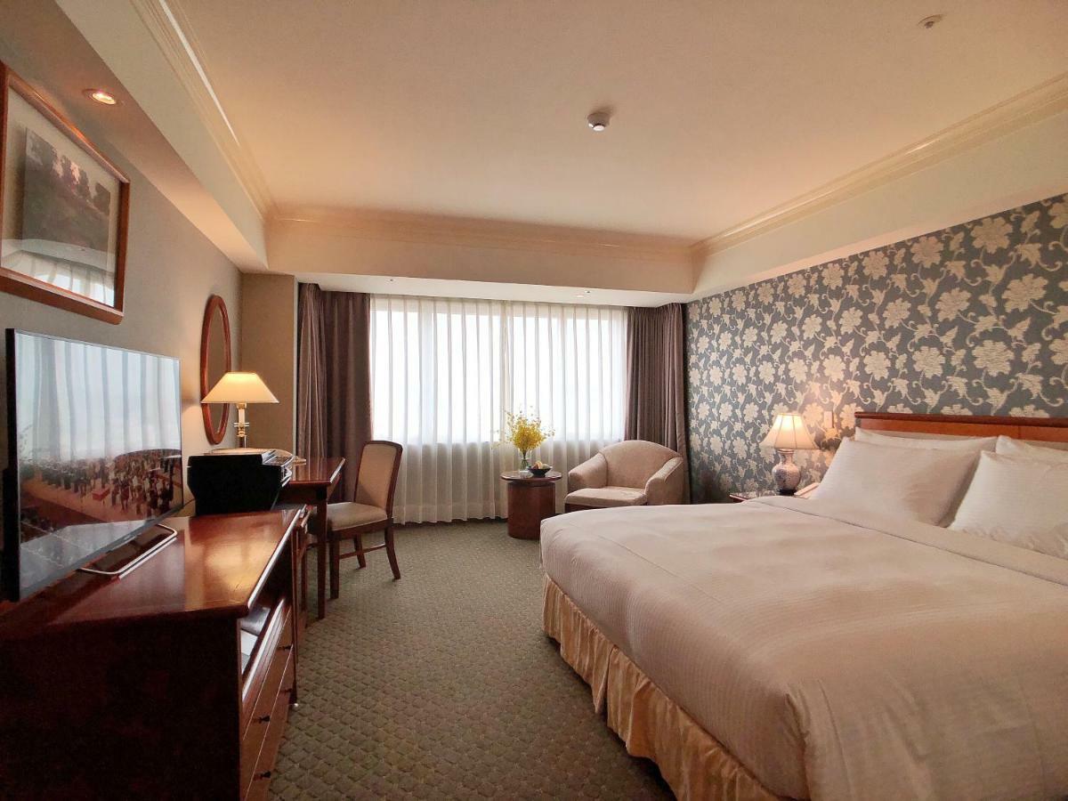 Evergreen Laurel Hotel - Тайджун Екстериор снимка The photo shows a hotel room with a spacious layout. It features a large bed with white bedding, bedside lamps, and a decorative headboard. There is a comfortable seating area with an armchair and small table. A desk is present, complete with a lamp 