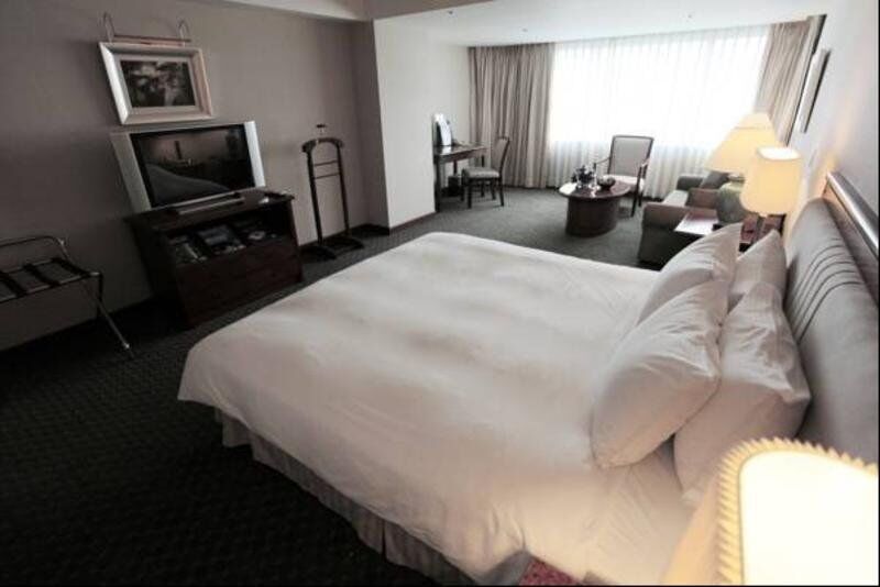 Evergreen Laurel Hotel - Тайджун Екстериор снимка The photo shows a hotel room featuring a large bed with white bedding. There is a flat-screen television on a wooden cabinet opposite the bed. Nearby, there are two armchairs and a small table, creating a cozy seating area. Large windows allow natura