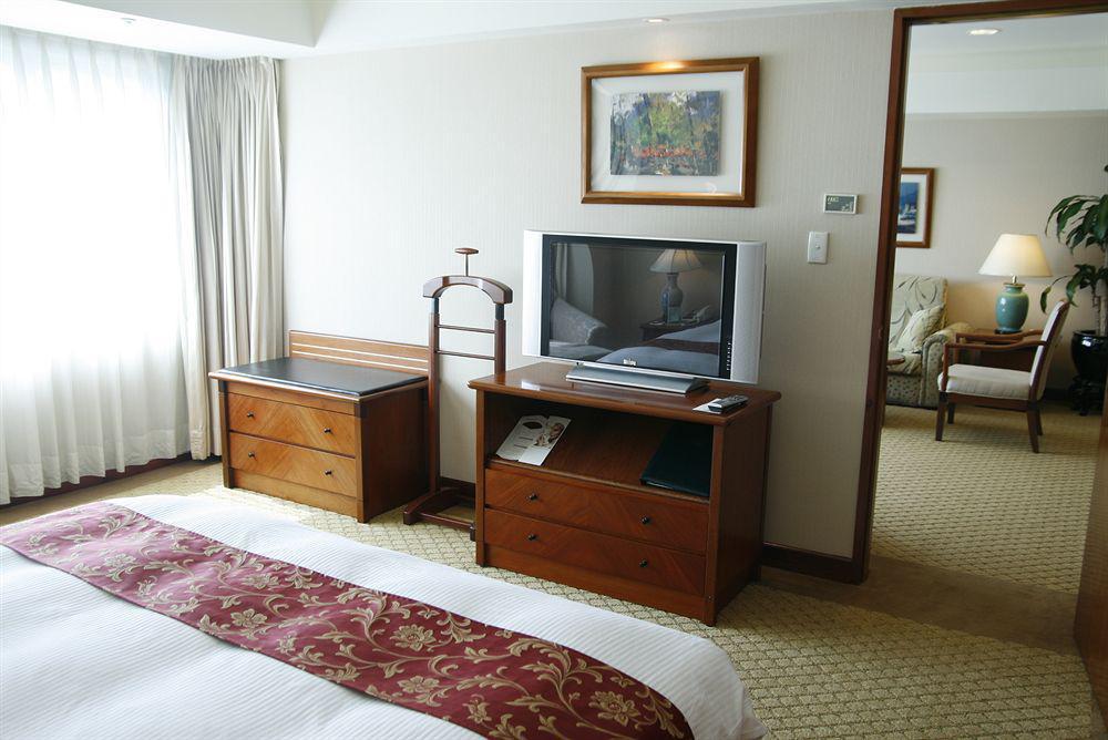 Evergreen Laurel Hotel - Тайджун Екстериор снимка The photo depicts a hotel room interior. In the foreground, there is a neatly made bed with a decorative red bedspread. To the left, a large window allows natural light to fill the room, with light-colored curtains drawn to one side. 

Next to the be