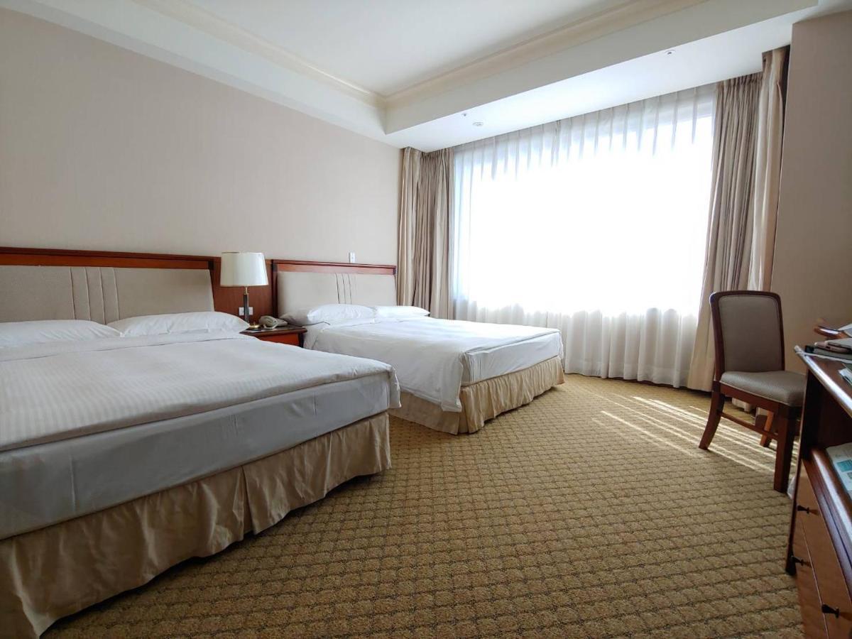 Evergreen Laurel Hotel - Тайджун Екстериор снимка The photo shows a neatly arranged hotel room featuring two beds: one double bed and one single bed. The room has beige walls and a warm color palette. Large windows with sheer curtains allow natural light to flood in, creating a bright and airy atmos