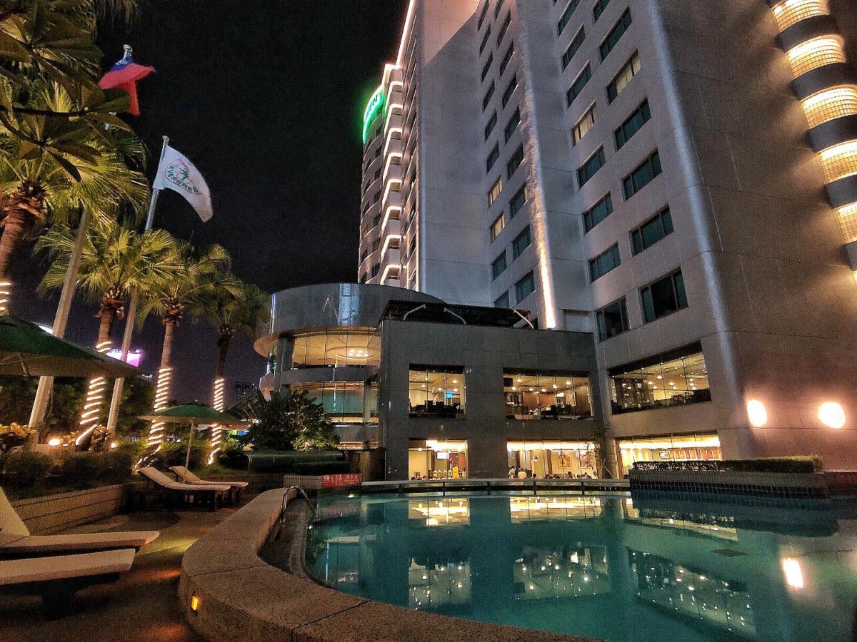Evergreen Laurel Hotel - Тайджун Екстериор снимка The photo depicts a modern hotel or building at night, featuring a sleek facade illuminated by lights. In the foreground, there is a swimming pool that reflects the surrounding lights and palm trees. There are lounge chairs near the pool, and the atm